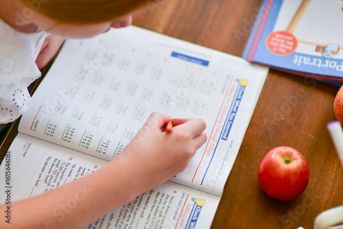 Quadro su tela A young girl focuses on solving math problems in her workbook during a homeschool lesson