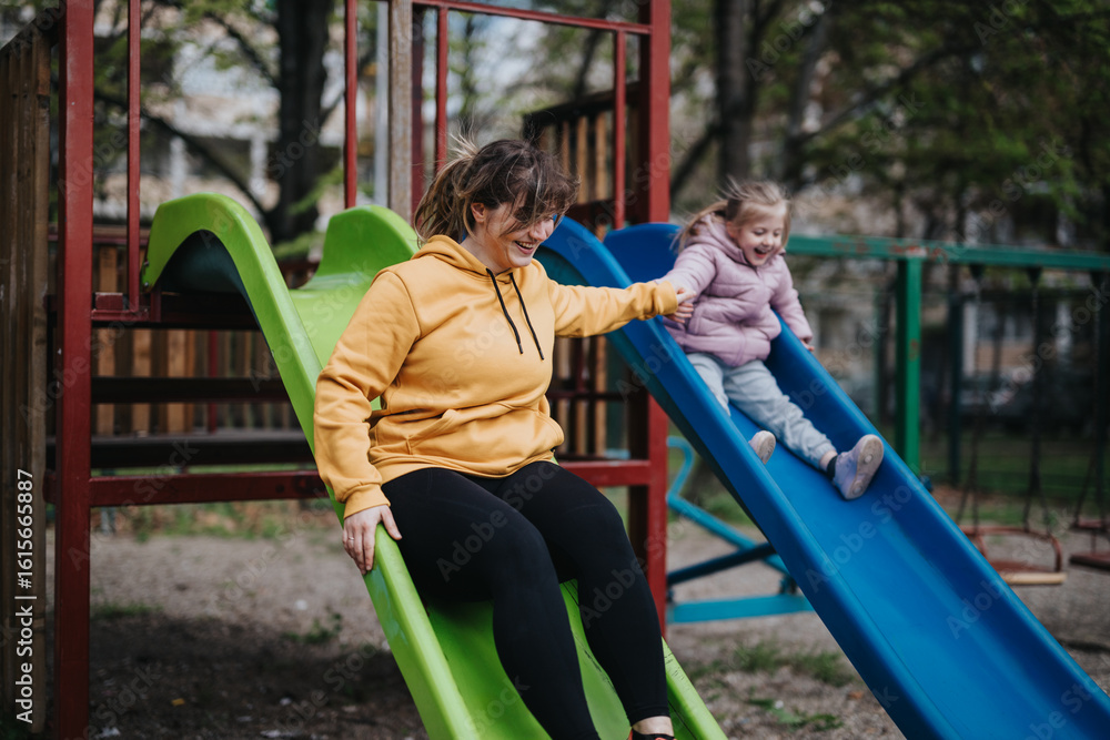 Fototapeta premium A cheerful mother and her young daughter enjoying sliding at a park, sharing a joyful moment.