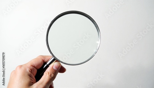 A hand holds a magnifying glass against a neutral background.