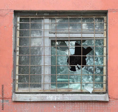 Broken glass in a barred window in a red wall