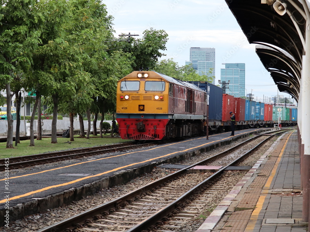 Fototapeta premium Rail Freight: A powerful freight train rolls along the tracks, transporting shipping containers through an urban landscape, showcasing the efficiency and scale of modern transport