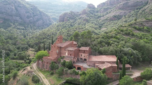 Wallpaper Mural Aerial view of buildings nestled in a lush forest with mountains, contrasting red brick with green canopy, El Marquet de les Roques, Spain. Torontodigital.ca