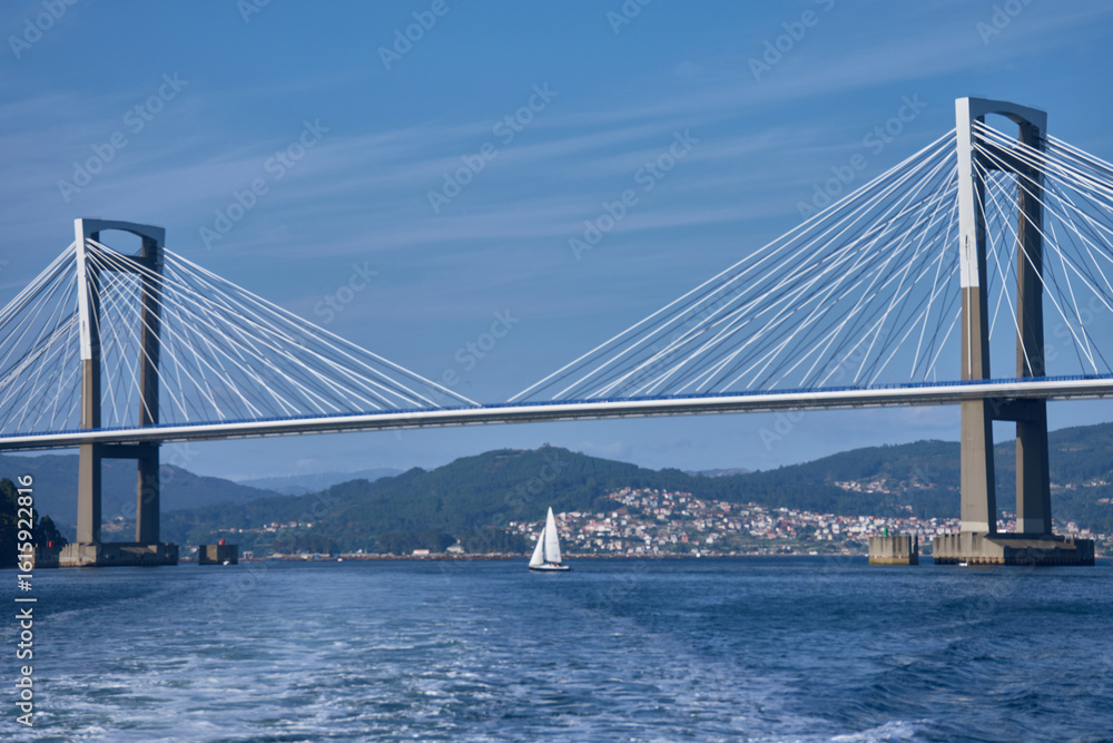 Fototapeta premium Sea wake in the foreground as a boat moves away, leaving Rande Bridge behind in the Vigo Estuary on a clear day