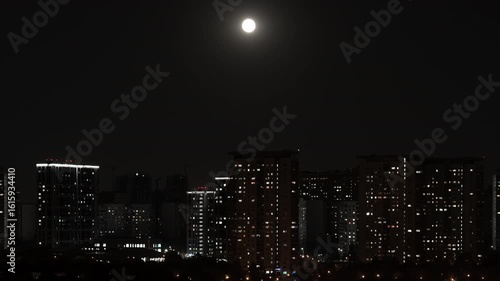 Time lapse. Rising moon over a big city at night. Hundreds of lights come on and go out in houses