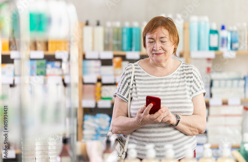Senior woman looking at shop windows in pharmacy with phone. Client scrolls through list of reminders and notes on phone. Electronic prescription set of medications, drugs to strengthen immune system.