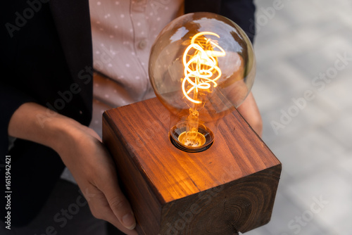 Innovative business idea presentation concept – corporate employee (woman) holding glowing lightbulb symbolizing creativity, startup energy, and visionary thinking in action