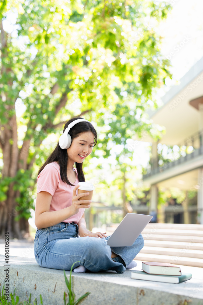 Young female student with laptop and headphones studying online sitting outdoor drinking coffee at university campus. Young female student with laptop and headphones studying online sitting outdoor drinking coffee at university campus.