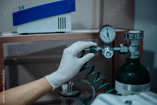 Gloved hand adjusting pressure valve on gas cylinder in medical lab, ensuring safe flow.