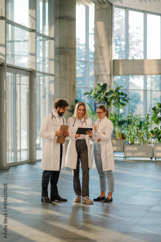 Fototapeta premium Medical team using tablet and discussing patient chart in hospital lobby