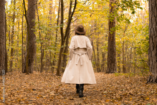 Tableau sur toile Back view of an elegant woman in a coat and wide-brimmed hat walking alone throu