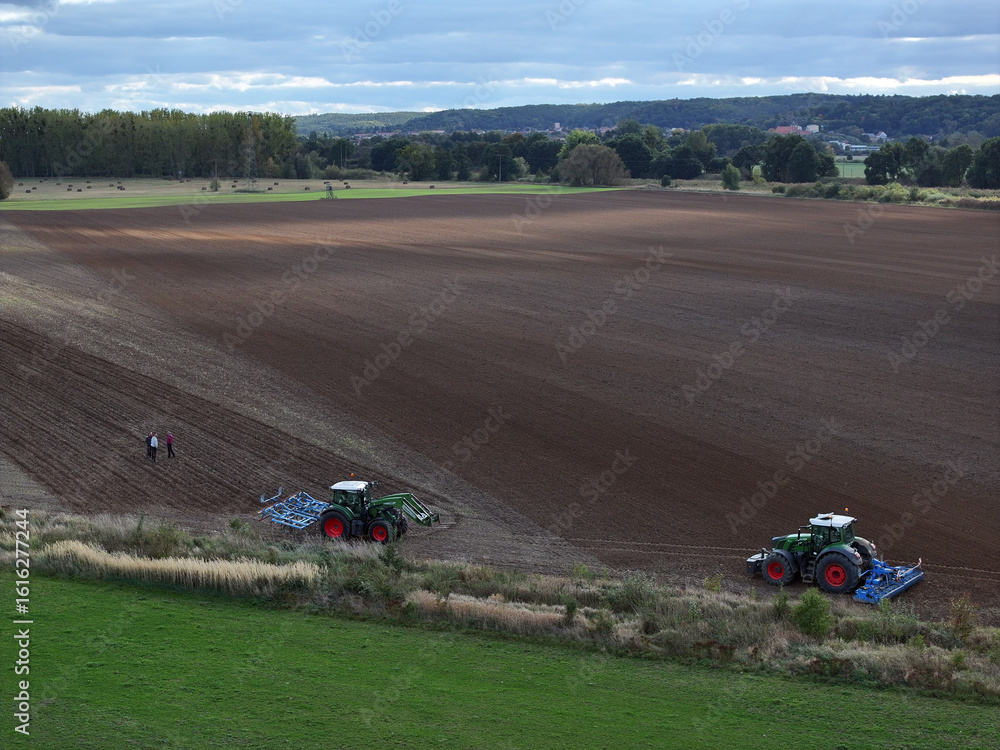 Aerial view of tractors tilling the rich, dark earth in a vast field near Bralitz, contrasting with the vibrant green of the surrounding grass, Bad Freienwalde, Brandenburg, Germany. Aerial view of tractors tilling the rich, dark earth in a vast field near Bralitz, contrasting with the vibrant green of the surrounding grass, Bad Freienwalde, Brandenburg, Germany.