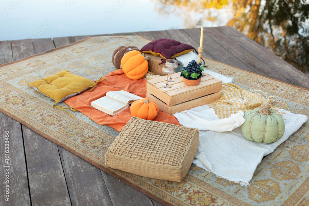 Φωτογραφία Aesthetic boho autumn picnic on the Pierce with Lake with pumpkins, carpet, plaid, cushions, fall decor, book, fruits, table with glasses