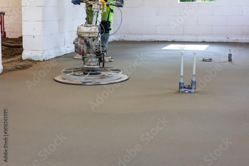 Concrete Floor Smoothing with Power Trowel in New Building, Worker using power trowel machine to smooth freshly poured concrete floor during interior construction of a modern residential house.