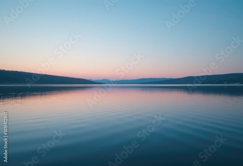Still lake at dawn with silhouetted mountains reflecting a pink and blue sky