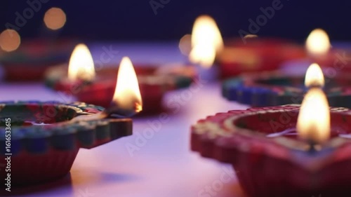 Close up of several diya lamps with flames on a table in a dimly lit setting indoors scene