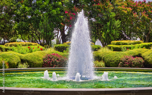 A large fountain with a white spout is surrounded by a lush green garden