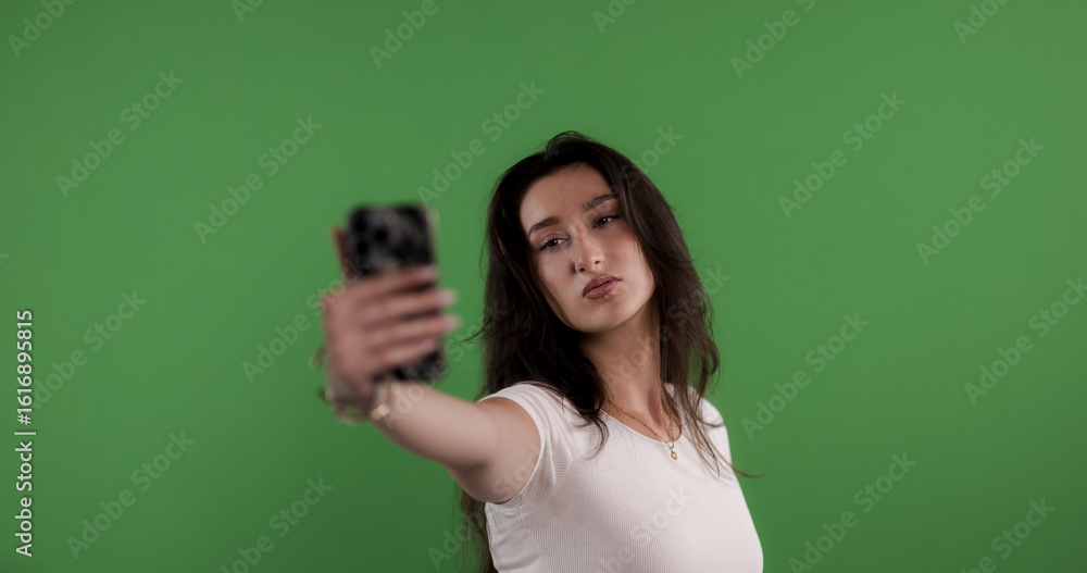 Fashion model taking a selfie with smartphone on green screen background Fashion model taking a selfie with smartphone on green screen background