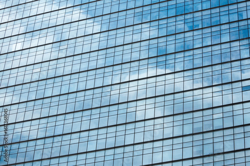 Glass mirror skyscraper wall with blue sky and white clouds reflection close up