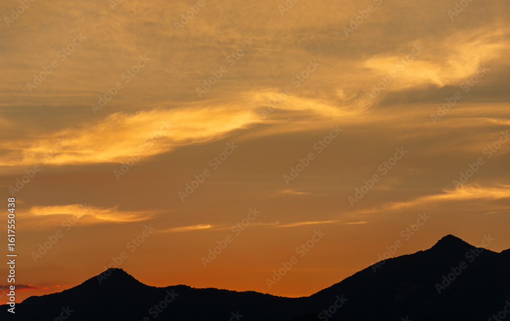 Obraz premium Golden Sunset Clouds Above Silhouetted Mountain Peaks