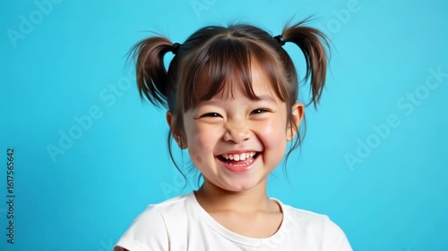 Playful young girl with pigtails giggling joyfully against vibrant sky blue backdrop, capturing pure childhood happiness