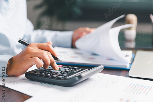 Office businesswoman hand to operate calculator analyzing financial data, counting costs on desk. accounting, financial analysis for business budget planning, calculation support, finance management.