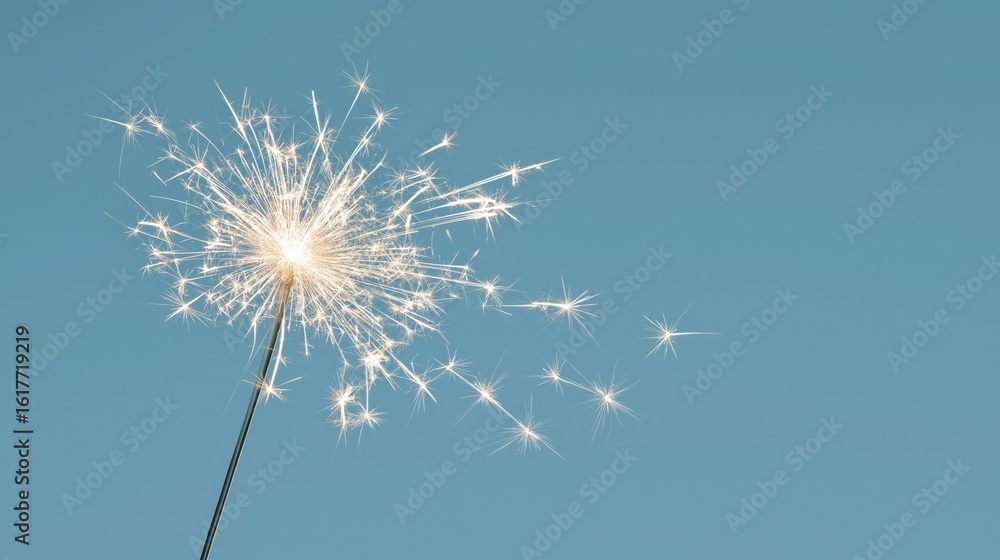 Naklejka premium Sparkler ignites with bright white sparks against a clear soft blue sky