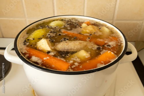 Homemade chicken broth with vegetables in white pot