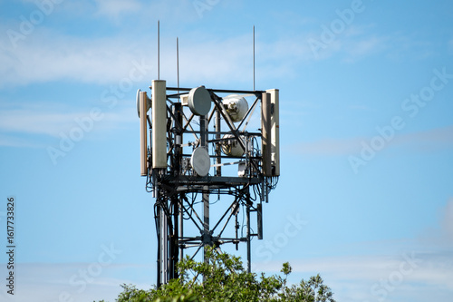 A mobile communication tower surrounded by green treetops under a bright blue sky. Modern technology and connectivity.