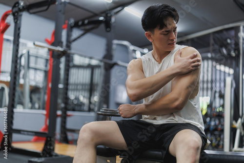 Fototapeta Young athlete experiencing shoulder pain after workout in gym