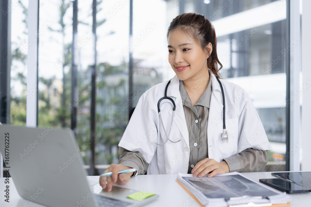 portrait of a confident female doctor using laptop sitting at working desk in hospital, Medical and health care concept. portrait of a confident female doctor using laptop sitting at working desk in hospital, Medical and health care concept.
