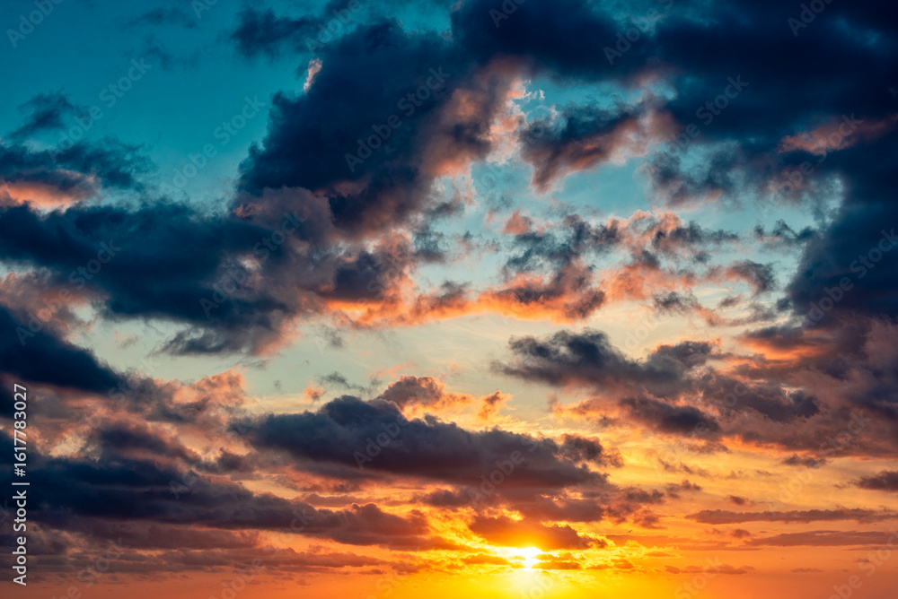 Fototapeta premium Sonnenunter- oder Aufgang am Horizont mit teilweiser verdeckter Sonne bei aufgelockerter Bewölkung im warmen Gegenlicht der Sonne