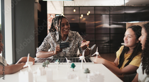 Black female teacher teaches and instructs primary girls group students, clean energy lesson at learning table in science classroom, discusses experiment knowledge for children of elementary school.