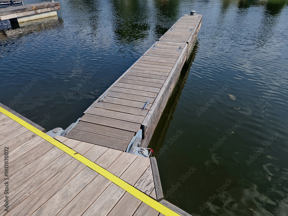 Fototapeta premium anchoring concrete footings hold the concrete floating pier by the metal rods. chains and ropes as insurance in case of flood. wooden paneling and coarse mesh as railings