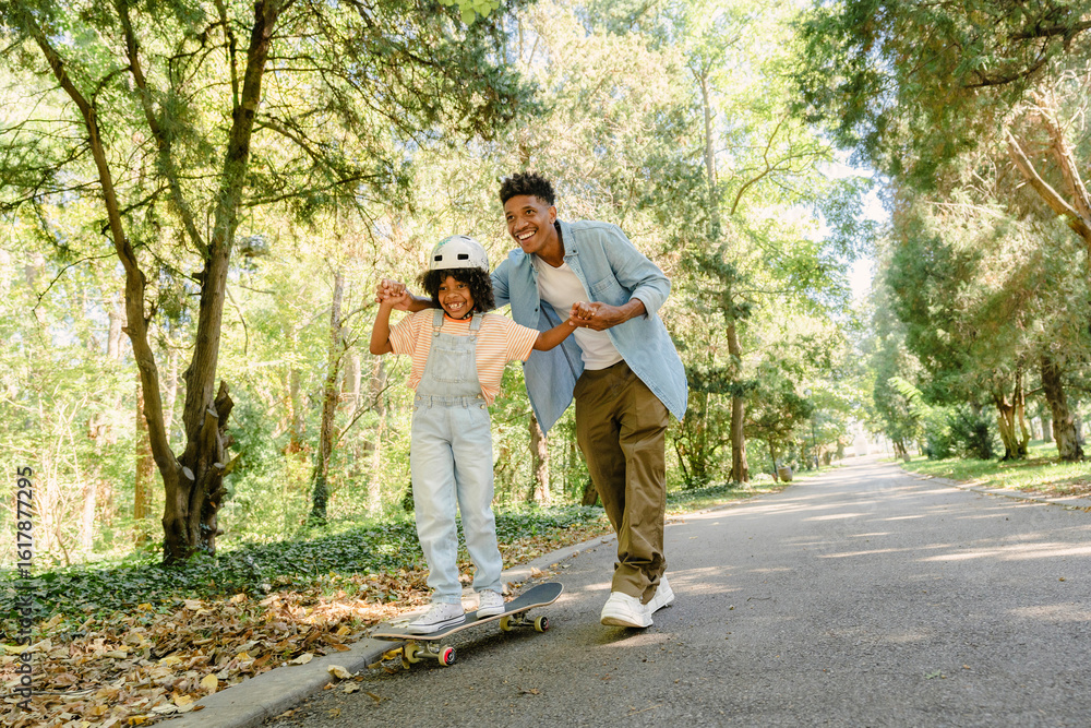 Father supporting daughter learning to skateboard in sunny park Father supporting daughter learning to skateboard in sunny park
