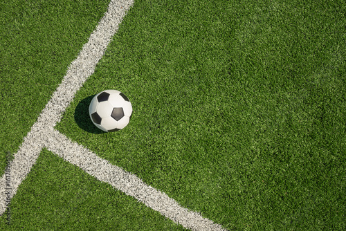 Soccer ball on green grass field with white line corner. Football stadium background. View from above.