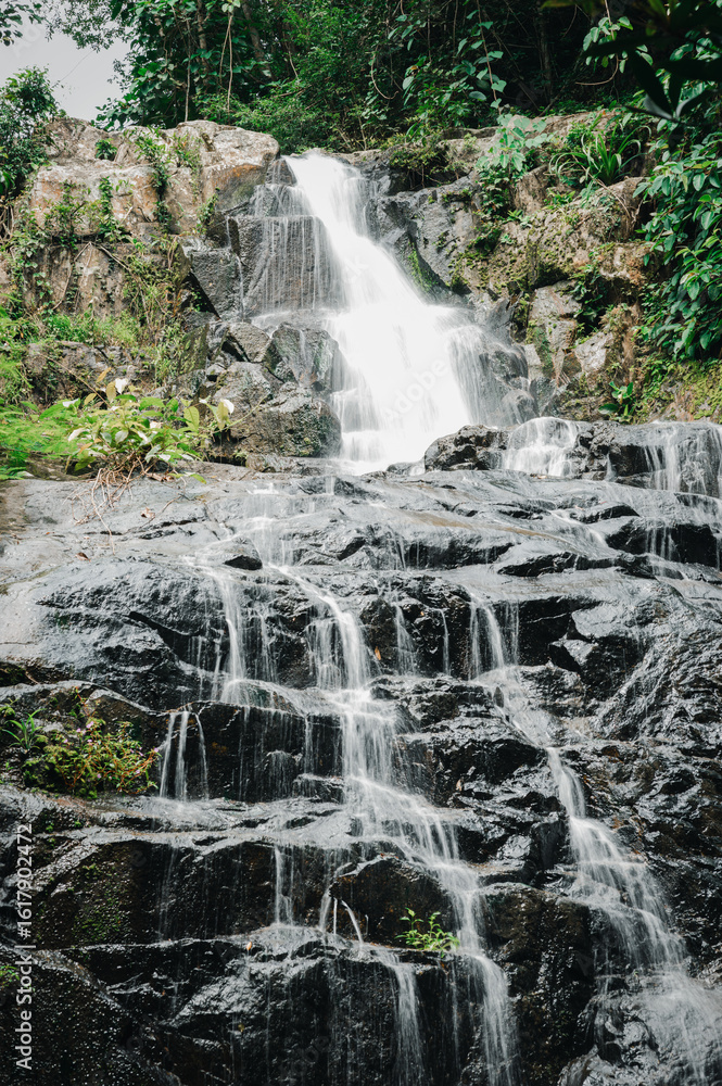 Obraz premium Serene Waterfall Cascading Over Rocky Terrain in Lush Greenery