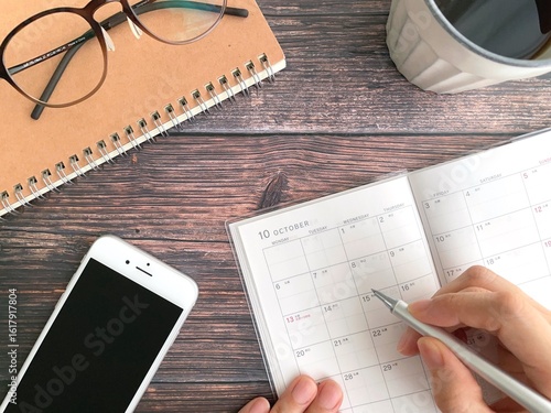 10月のスケジュール帳に記入する女性の手と机上のスマホ