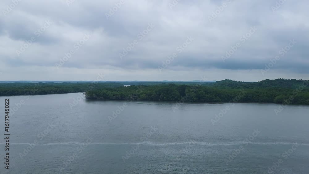 Aerial view of the Panama Canal with lush rainforest and river bend under a dramatic cloudy sky. Aerial view of the Panama Canal with lush rainforest and river bend under a dramatic cloudy sky.