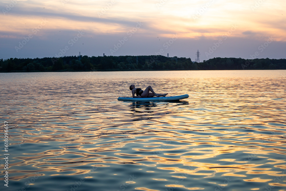 Naklejka premium Woman practicing SUP yoga, relaxing on a paddle board. Woman on sup board.