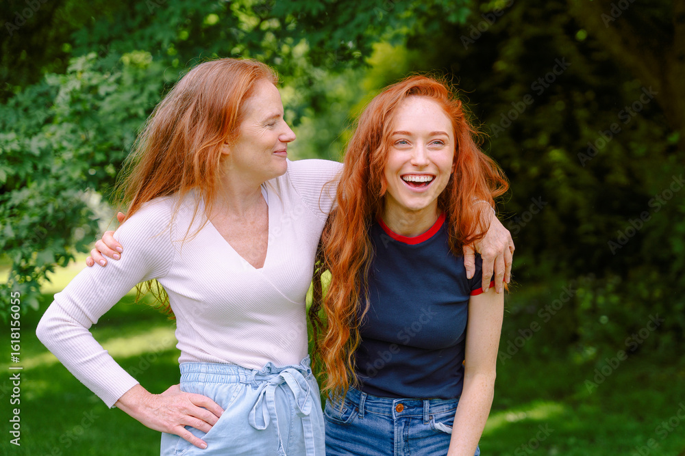 Obraz premium Two red-haired women mother, daughter enjoying a joyful moment together in a lush green park on a sunny afternoon, sharing laughter and friendship with a warm atmosphere