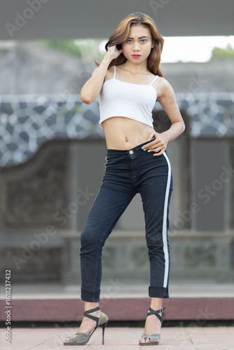 Trendy Woman in White Tank Top and Dark Jeans : A fashionable young woman wearing a simple white spaghetti strap tank top and stylish dark wash jeans