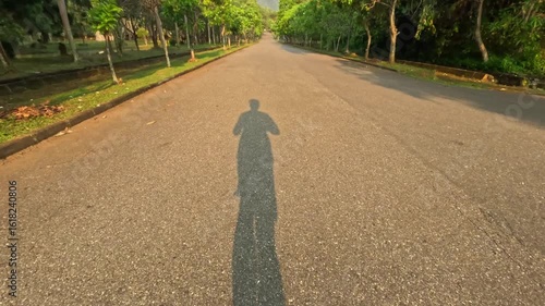 point of view of man shadow running or jogging on asphalt road in the afternoon