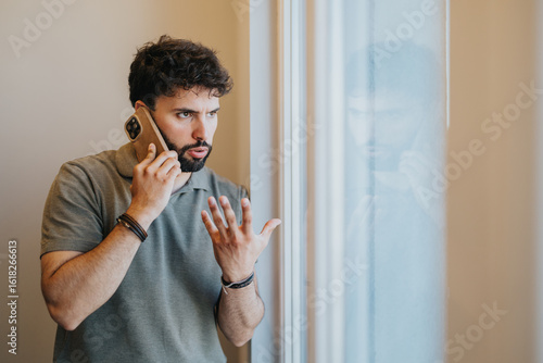 Bilde på lerret A man standing near a window making a phone call, exhibiting concern or question