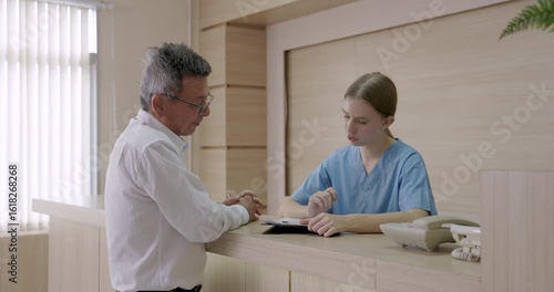Slowmotion scene of hospital billing interaction with asian male preparing credit card payment while young female nurse handling medical charge process at reception counter
