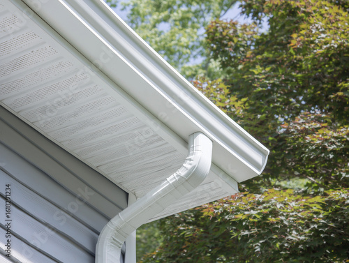 White gutter guard system, fascia, drip edge, soffit, and downspout strap with horizontal vinyl siding at an upscale single-family home neighborhood
