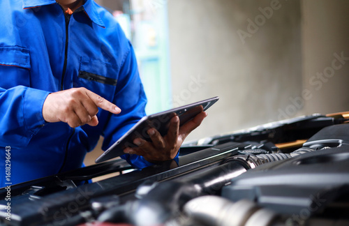 Mechanic standing inspecting car with laptop checking performance and operation of car. Maintenance topic for service, vehicle check up, customer service.