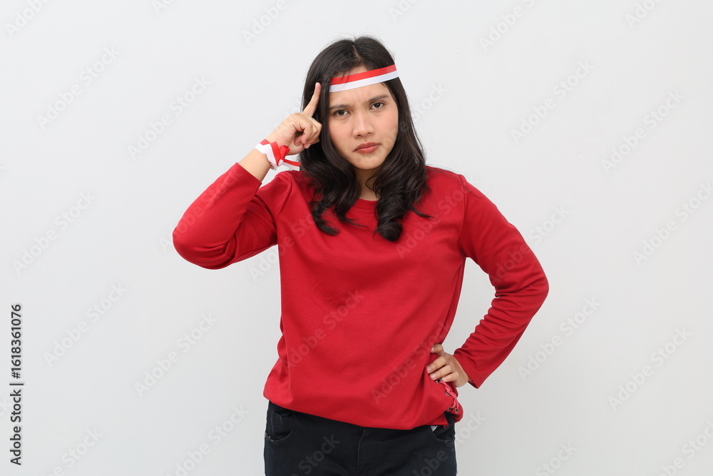 Indonesian woman with red and white ribbon celebrating Indonesian independence day, serious expression, thinking gesture while holding forehead, standing looking at camera. Indonesian woman with red and white ribbon celebrating Indonesian independence day, serious expression, thinking gesture while holding forehead, standing looking at camera.