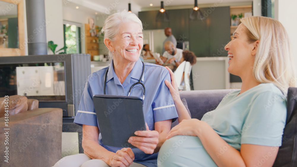 Obraz premium Senior Midwife With Digital Tablet Visiting Pregnant Woman At Home With Family In Background