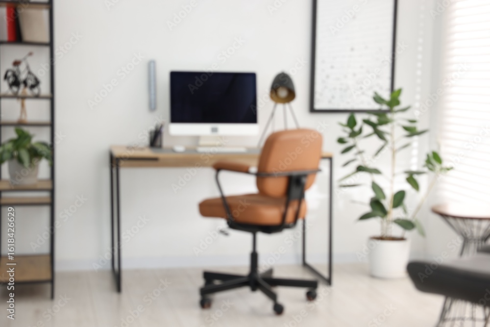 Fototapeta premium Blurred view of workplace with wooden desk, lamp and computer indoors
