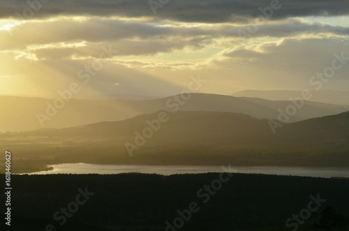 Sunbeams shine through a cloudy sky over Loch Morlich and Glenmore Forest Park in the Cairngorms National Park Scotland UK.